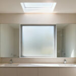 Bathroom with abundant natural light, large window, and skylight designed for circadian rhythm harmony, featuring light-colored finishes and serene ambiance.