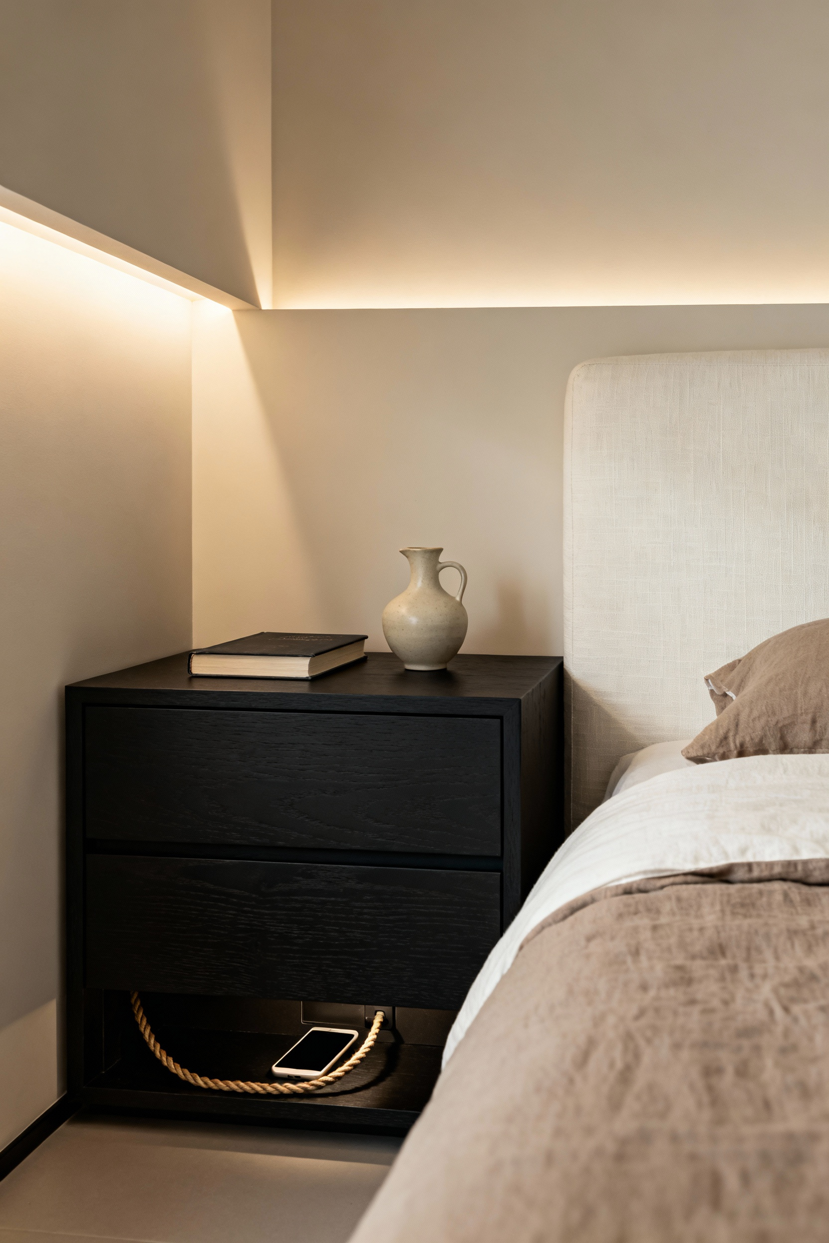 A serene, modern bedroom corner showcasing a digital detox perimeter layout. A dark wood nightstand with a closed drawer hides a charging smartphone, blocking blue light and securing the device away from view to promote better sleep hygiene.