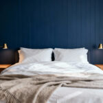 A deeply calming, modern bedroom featuring indigo blue paneled walls and crisp white bedding, emphasizing the psychological effect of low-luminance blue pigment.