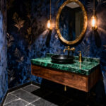 A small, luxurious powder room designed with dark midnight blue and gold geometric wallpaper, a walnut vanity, and emerald marble countertop, demonstrating the dramatic 'Jewel Box' design philosophy.