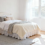 A high-key photograph showing the foundation of a flexible girl's bedroom, featuring soft white walls and neutral cream bedding, designed to be timeless and adaptable.