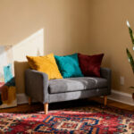 A photograph of a small rental apartment living room with beige walls, showcasing strategic non-permanent decorating ideas including a vibrant patterned area rug, colorful pillows, and large leaned artwork.