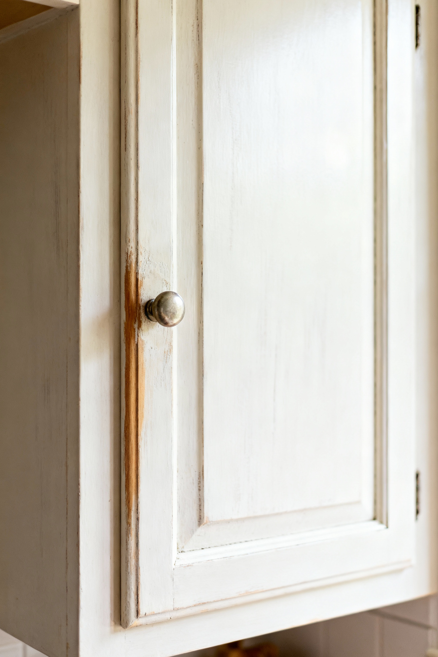Close-up of a farmhouse kitchen cabinet door with a naturally aged milk paint finish, showing authentic patina and subtle wear in soft natural light.