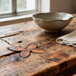 A rustic dining table featuring Wabi-Sabi design with aged, reclaimed wood, natural fissures, and butterfly joints. Handmade ceramics and linen add to the imperfect aesthetic.