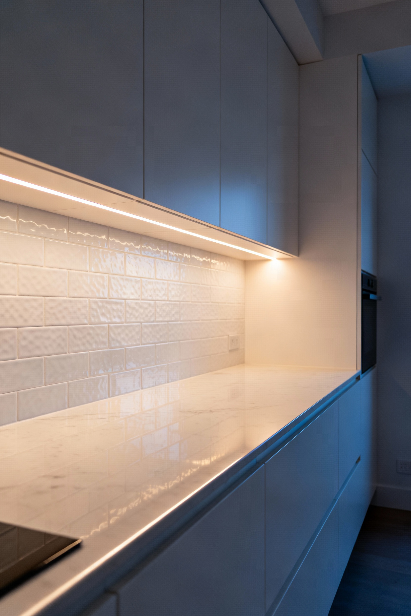 Modern small kitchen with integrated undershelf LED lighting casting a warm, diffused glow, eliminating shadows and visually expanding the countertop space, promoting openness and tranquility.