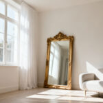A bright, airy apartment living room filled with natural light, featuring sheer white curtains, light-colored walls, a large gold-framed mirror reflecting light, and a modern minimalist sofa, creating a serene environment.