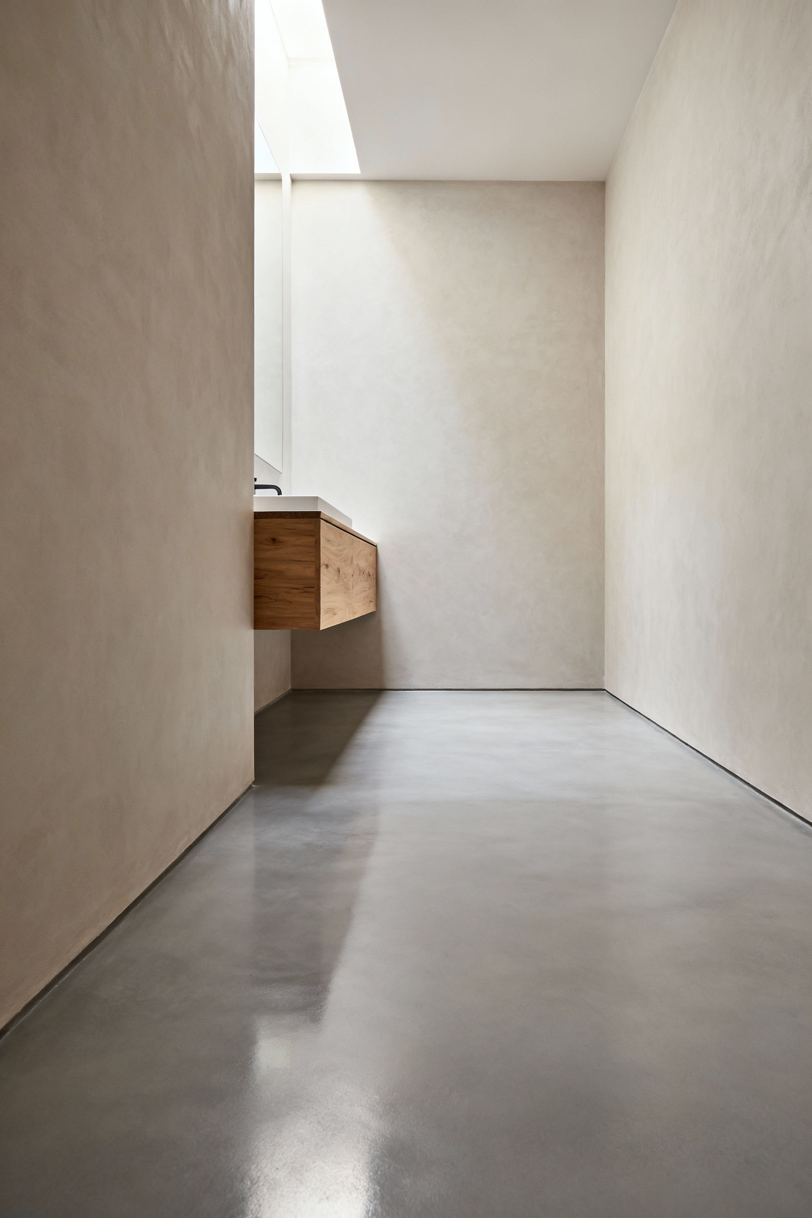 A minimalistic bathroom showcasing continuous light gray microcement flooring that seamlessly meets the textured walls, enhancing the visual spaciousness and tranquility of the design.
