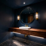 A small, sophisticated bathroom designed using deep matte charcoal blue paint on walls and ceiling to create an illusion of greater space and luxury, featuring a floating walnut vanity and brushed brass fixtures.