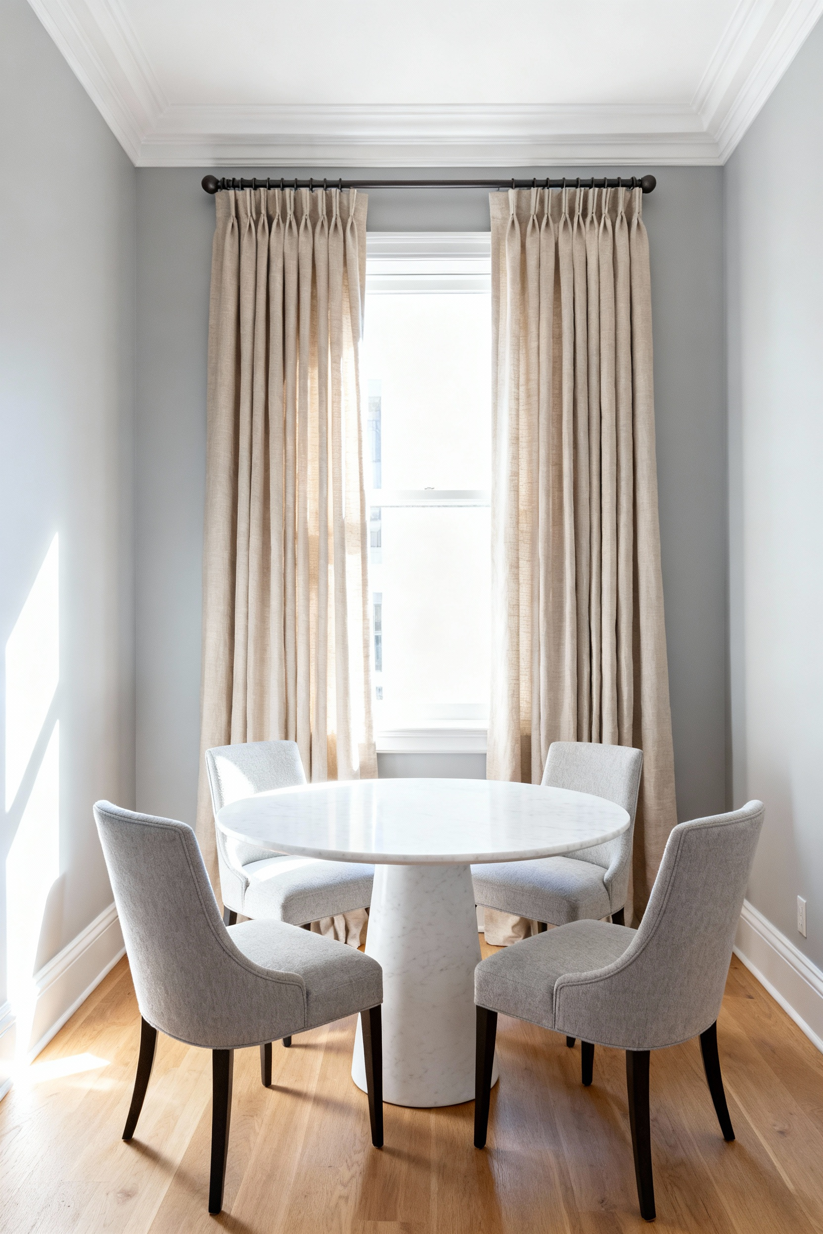 An elegant small dining room featuring luxurious oatmeal-colored floor-to-ceiling drapery mounted high near the crown molding, illustrating how vertical lines create the illusion of greater room height.