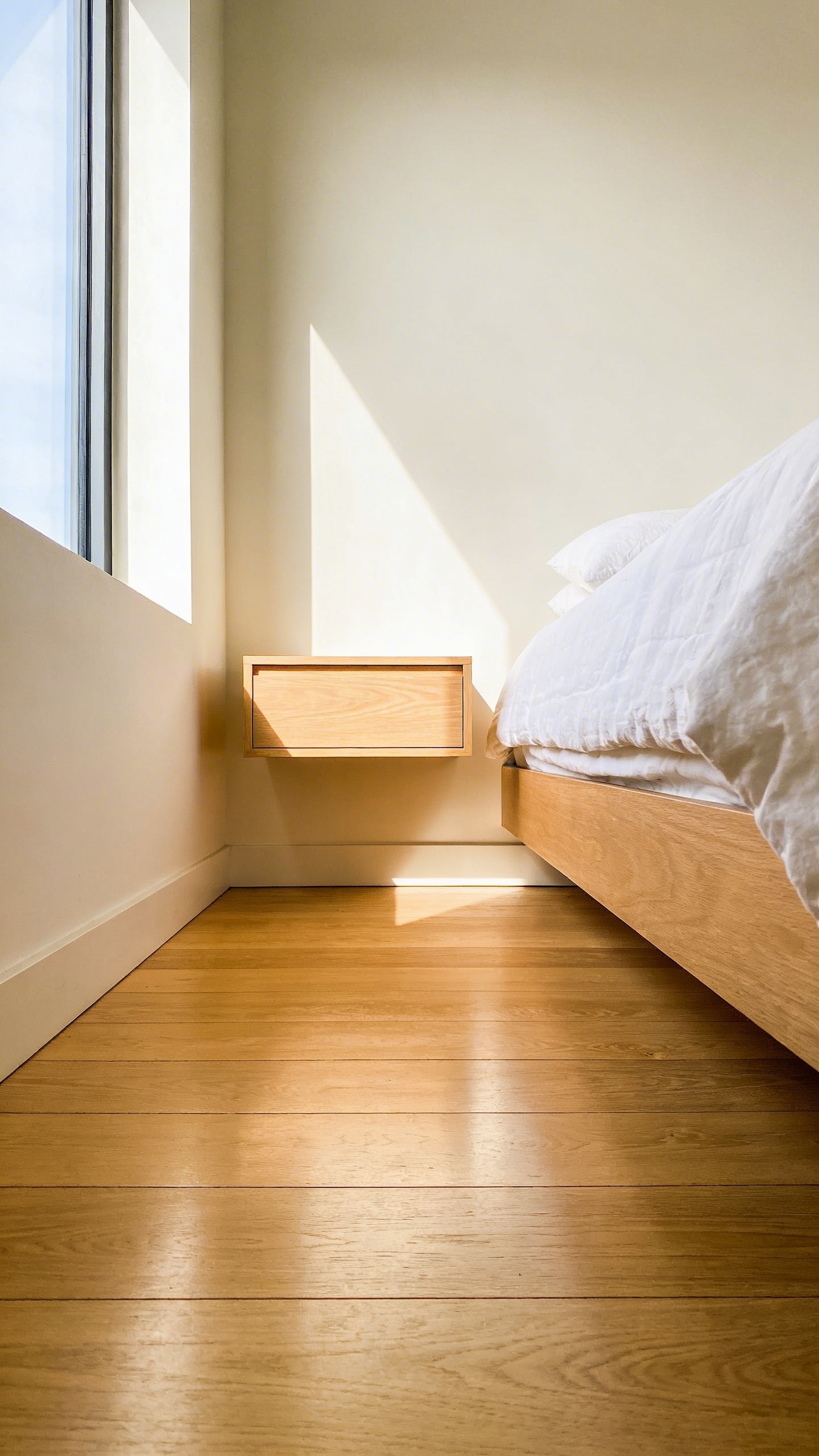A modern small bedroom featuring a floating wooden nightstand mounted to the wall to keep the floor area clear and open.