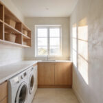 A bright and airy laundry room featuring textured limewash walls, natural oak cabinetry, and modern white appliances under a marble countertop.